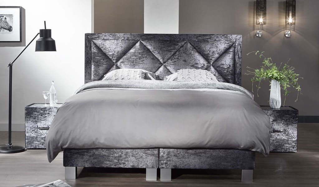Lit élégant avec tête de lit capitonnée grise, tables de chevet assorties, lampe moderne et vase de fleurs, dans une chambre contemporaine