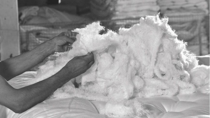 Mains manipulant du rembourrage blanc, probablement pour la fabrication artisanale de matelas ou de coussins, dans un contexte de mariage