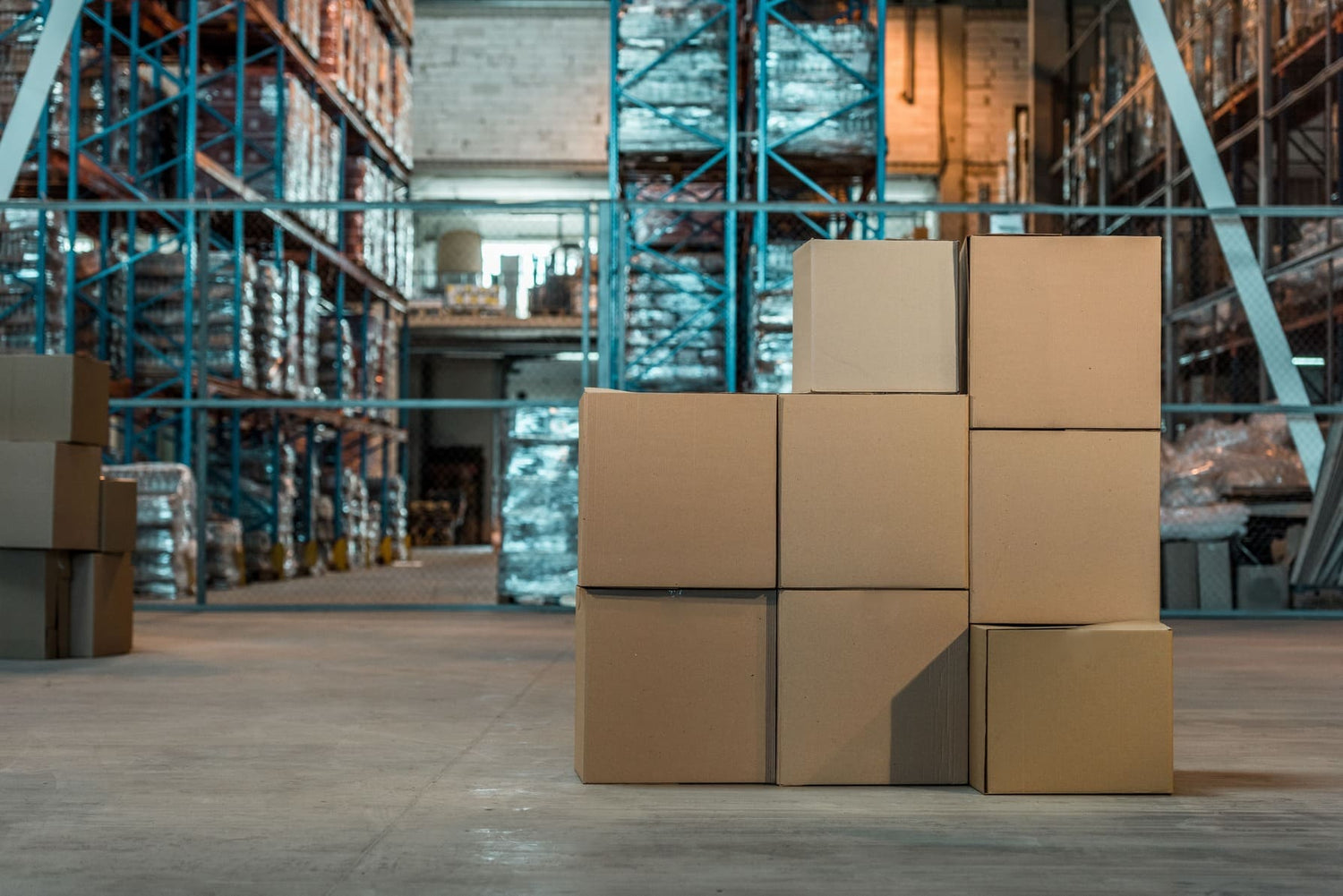 Cartons empilés dans un entrepôt avec des étagères métalliques en arrière-plan, illustrant un stockage industriel