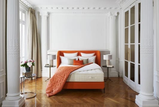 Chambre élégante avec lit orange, colonnes décoratives et parquet, ambiance impériale