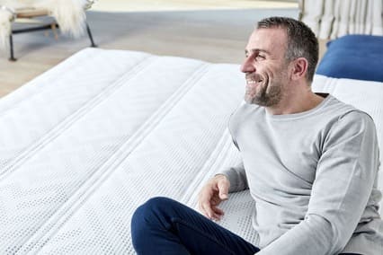 Homme souriant assis sur un matelas Lattoflex 2, dans un intérieur moderne et lumineux