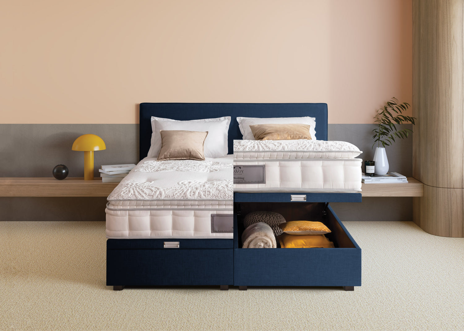 Lit avec tête de lit bleue, tiroir de rangement ouvert contenant des couvertures, dans une chambre moderne avec déco minimaliste