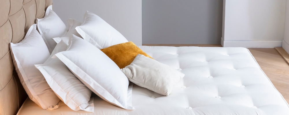 Oreillers blancs et un coussin jaune sur un lit avec une tête de lit capitonnée, dans une chambre moderne