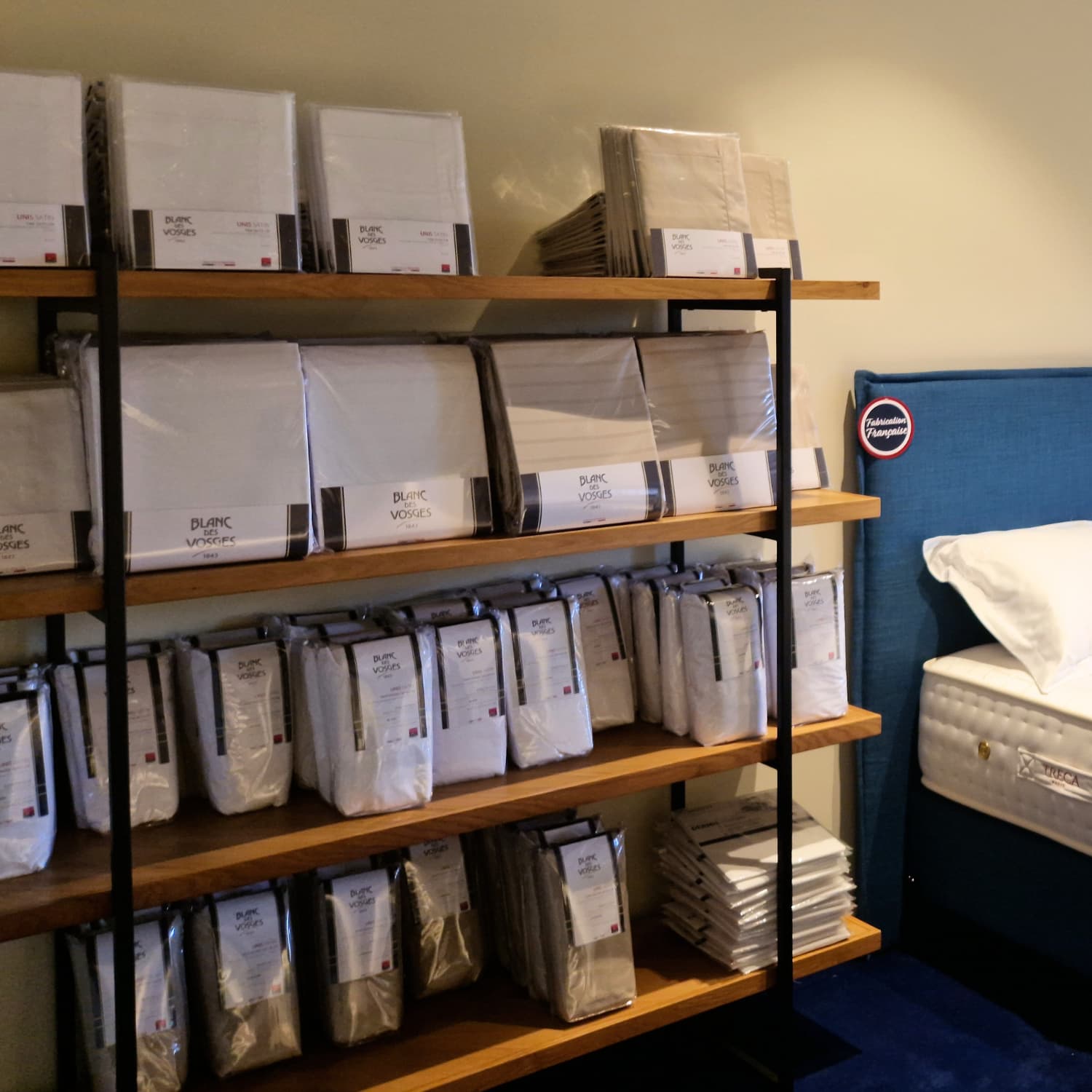 Présentoir de linge de lit en magasin, avec draps et housses de marque "Blanc des Vosges" sur étagères en bois