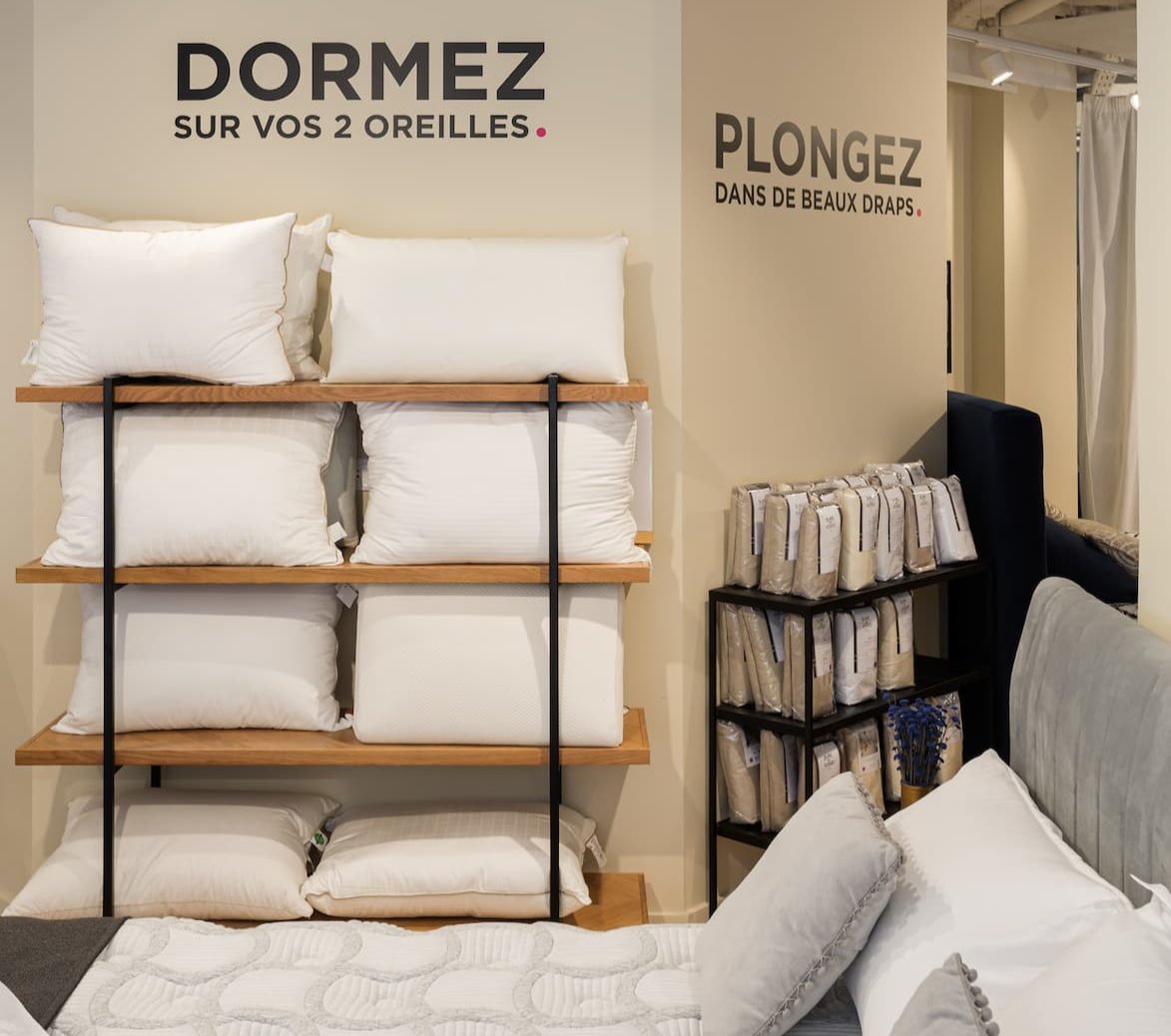 Oreillers blancs exposés sur des étagères en bois dans un magasin de literie, avec des slogans muraux sur le sommeil