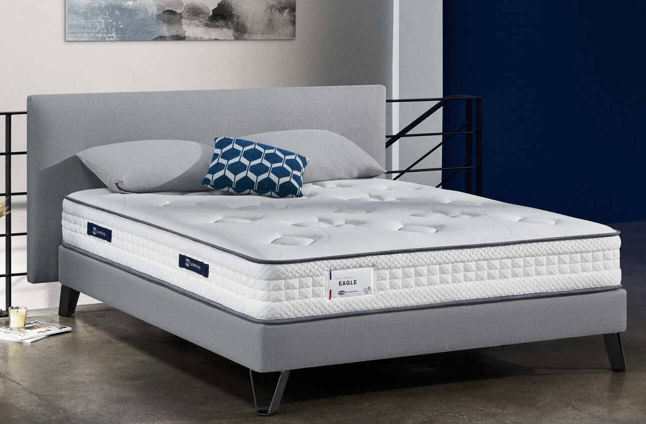 Lit Simmons Eagle avec matelas blanc et coussin bleu à motifs géométriques, dans une chambre moderne et élégante