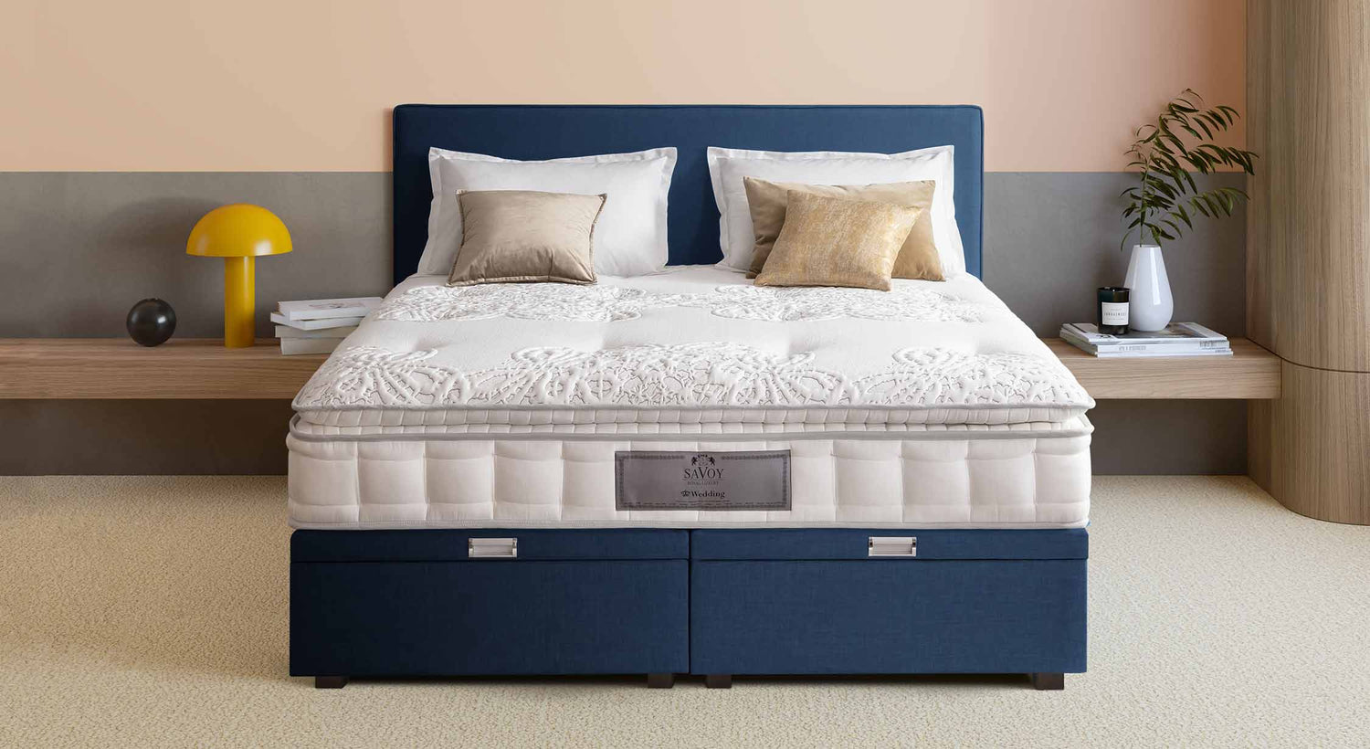 Lit avec matelas Savoy, tête de lit bleue, coussins beiges, lampe jaune et décoration moderne dans une chambre élégante