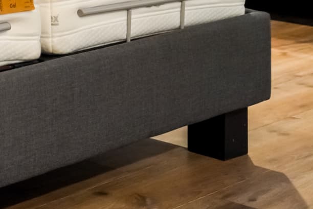 Pied de lit en bois sombre avec cadre de lit rembourré gris sur parquet