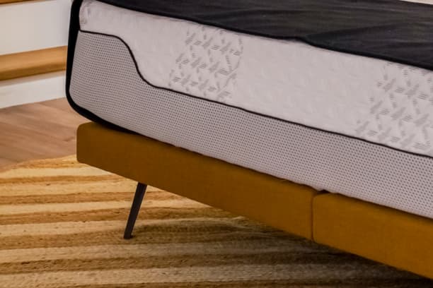 Pieds de lit modernes en métal noir sur un cadre de lit jaune, posés sur un tapis rayé