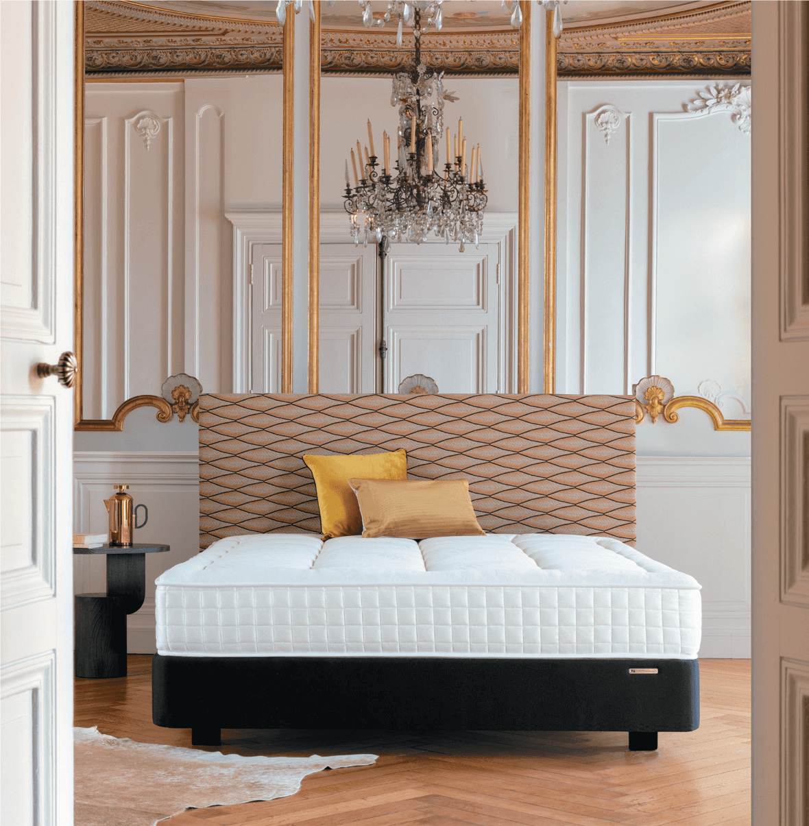 Lit élégant dans une chambre luxueuse avec moulures dorées et lustre, créant une ambiance sophistiquée et chaleureuse