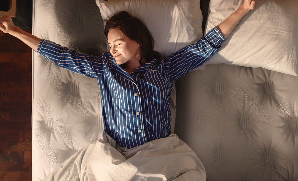 Personne s'étirant au réveil dans un lit, portant un pyjama rayé bleu, symbolisant le confort et le bien-être matinal