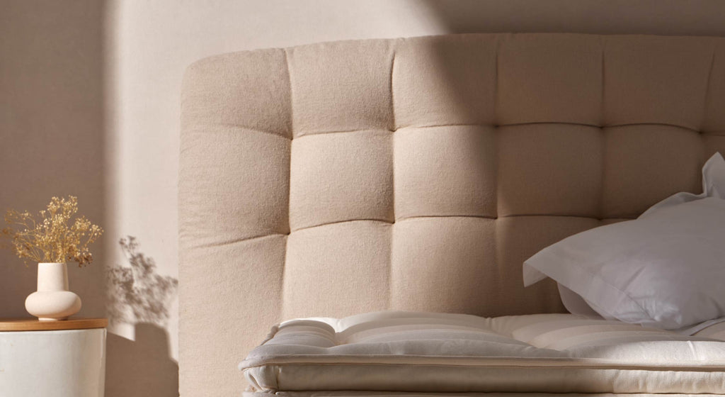 Tête de lit beige capitonnée avec oreiller blanc, ambiance douce et minimaliste, vase décoratif sur table de chevet