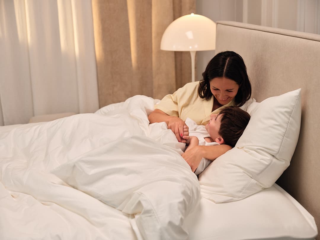 Mère et fils souriants allongés dans un lit, entourés de draps blancs, ambiance chaleureuse et intime