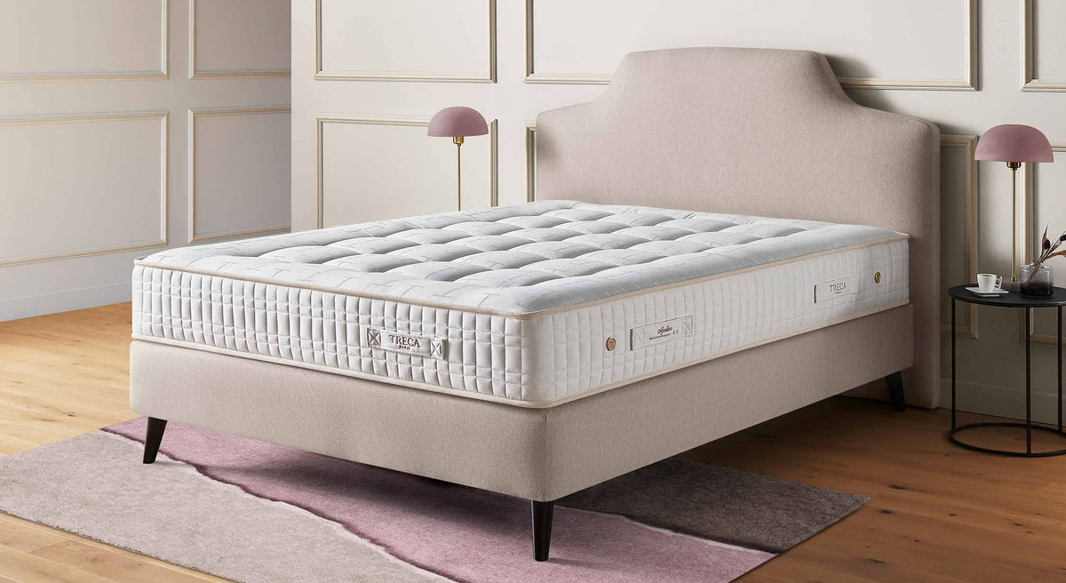 Matelas Treca Apollon sur un lit avec tête de lit beige, dans une chambre élégante avec lampes et table d'appoint