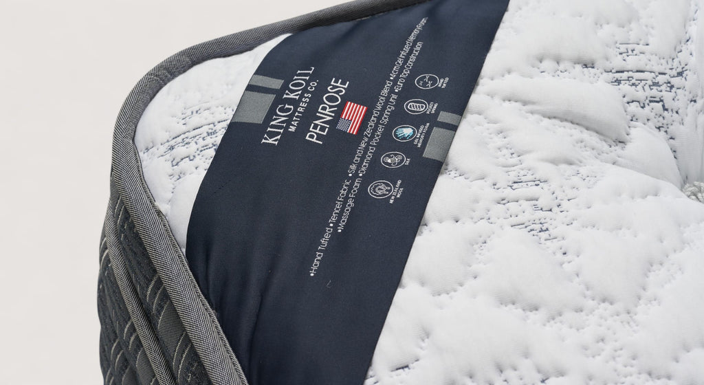 Étiquette du matelas King Koil Penrose avec détails de fabrication et matériaux, sur fond de tissu matelassé blanc