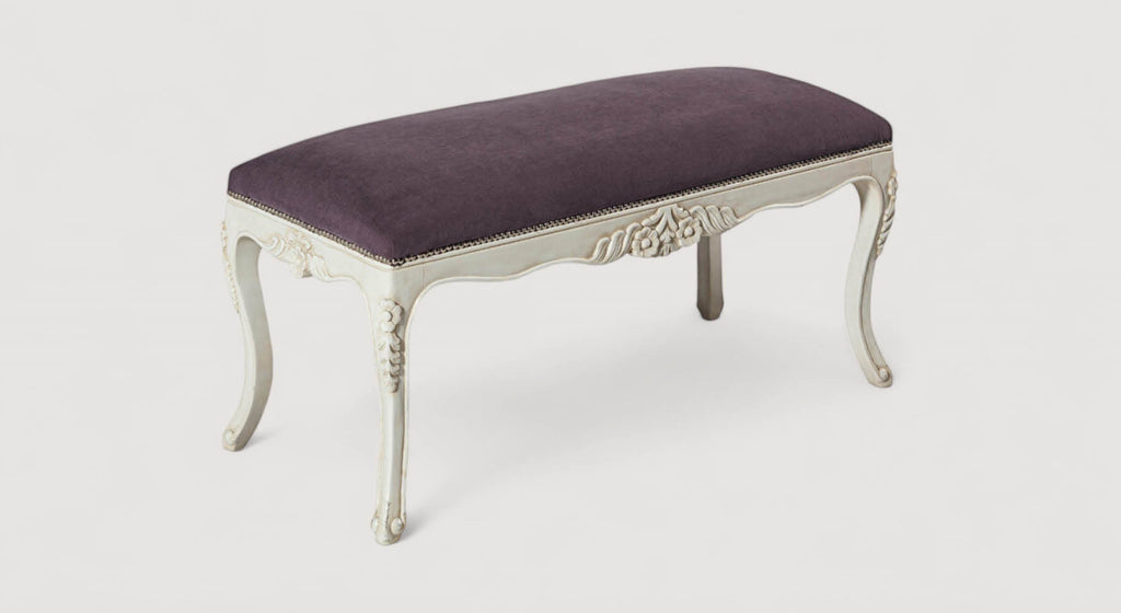 Banc de lit élégant avec pieds sculptés, assorti à un lit avec matelas texturé, dans une chambre lumineuse et moderne