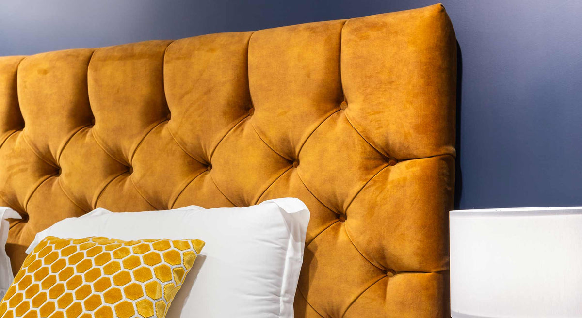 Tête de lit capitonnée en velours jaune moutarde avec coussin à motifs hexagonaux, ambiance élégante